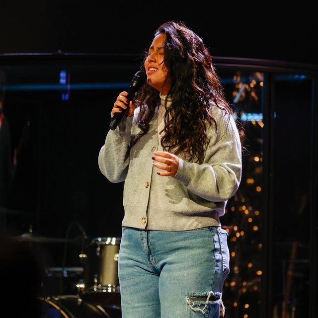Lala cantando en el escenario con un suéter gris